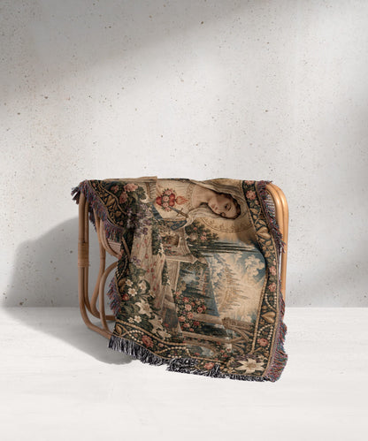 A woven tapestry throw blanket featuring a classic renaissance portrait draped over a rattan chair.