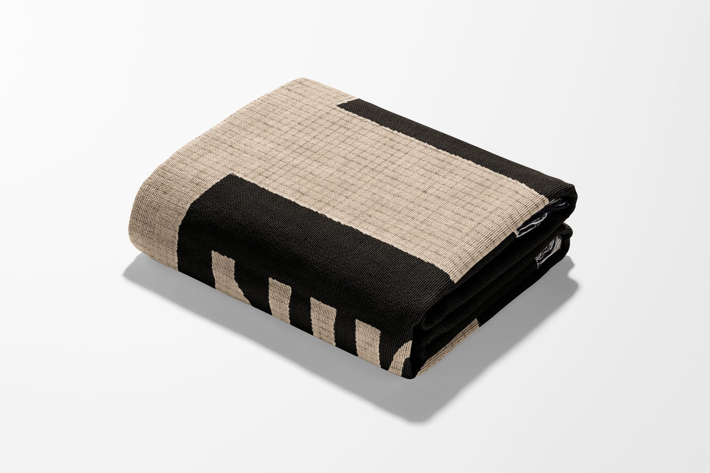 Folded blanket with black geometric stripes on a tan background.