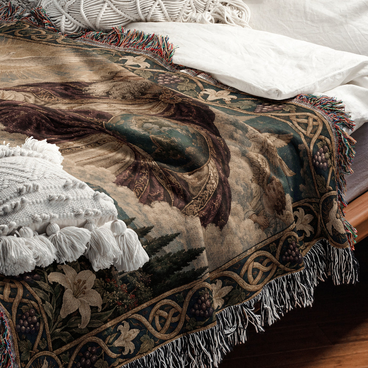 A folded tapestry-style throw blanket with floral and geometric borders and fringed edges rests on a bed.
