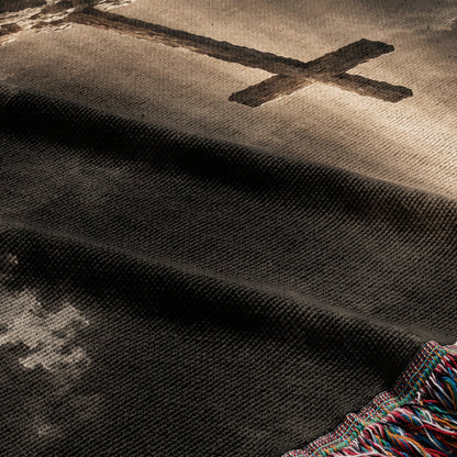 A folded black woven throw blanket with a large grey cross pattern and colorful fringed edges.