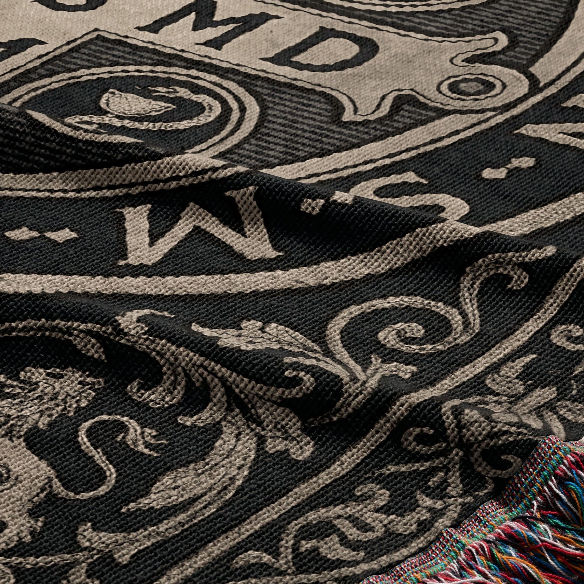 Black and tan woven blanket with ornate scrollwork and visible fringed edge.