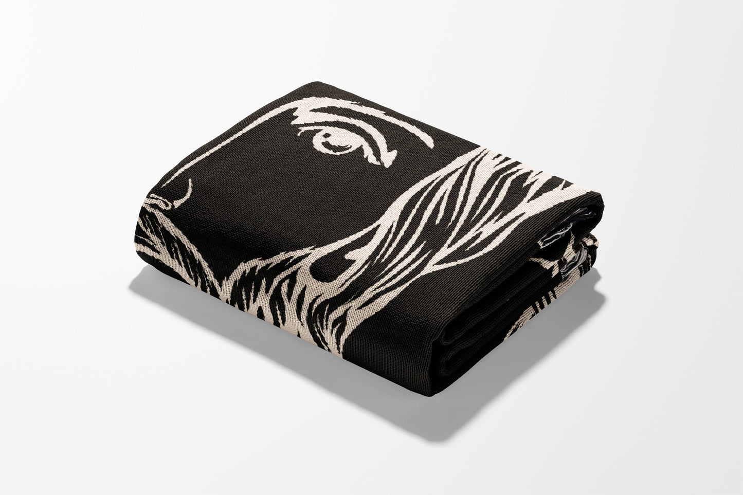 Folded black blanket with a cream-colored abstract face design.