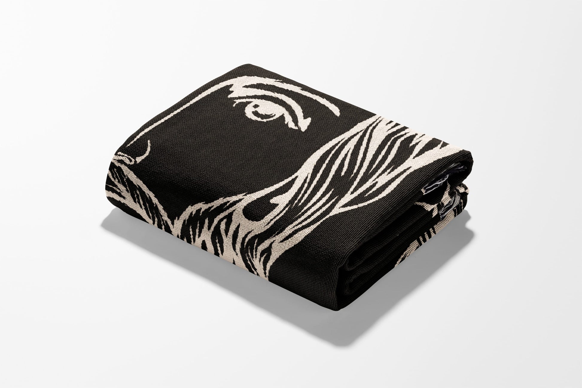 Folded black blanket with a cream-colored abstract face design.