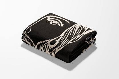 Folded black blanket with a cream-colored abstract face design.