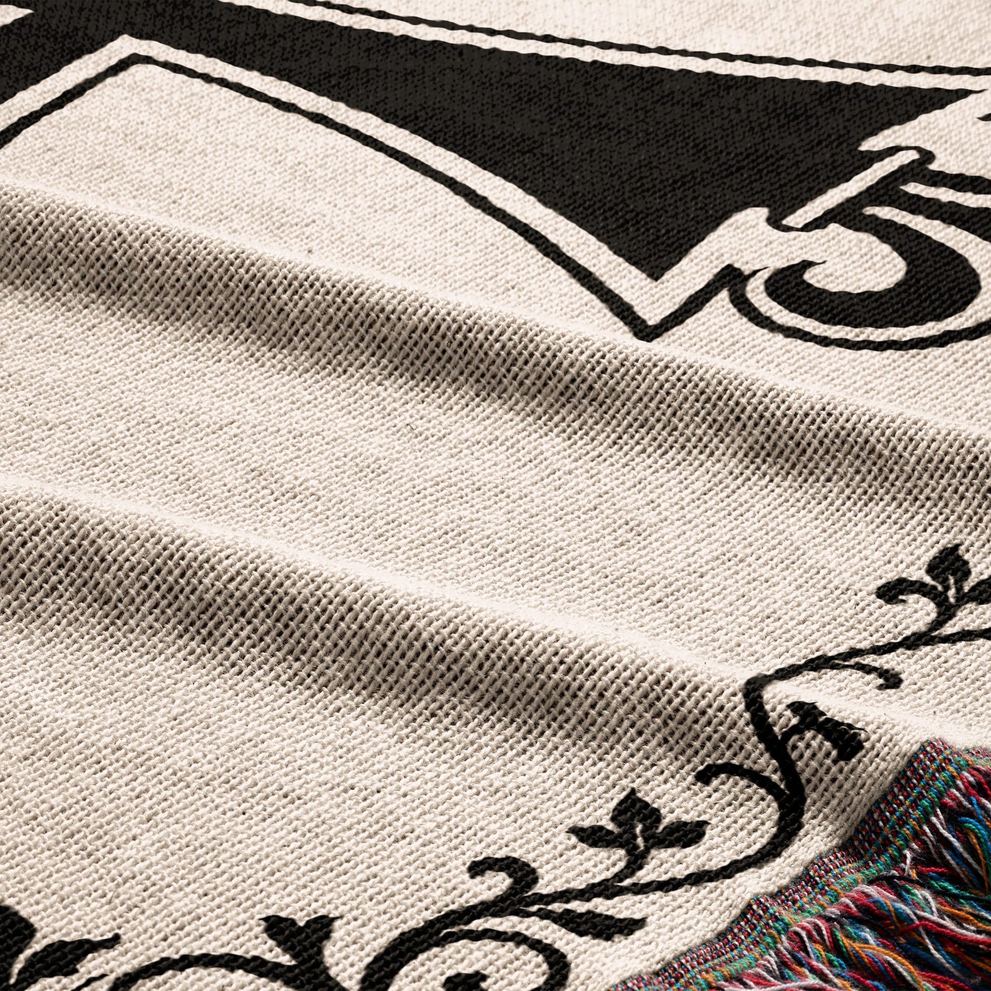Cream blanket with black ornate design and colorful fringe.