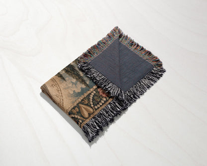 A folded woven throw blanket with fringe, showing both the patterned front and dark reverse side.