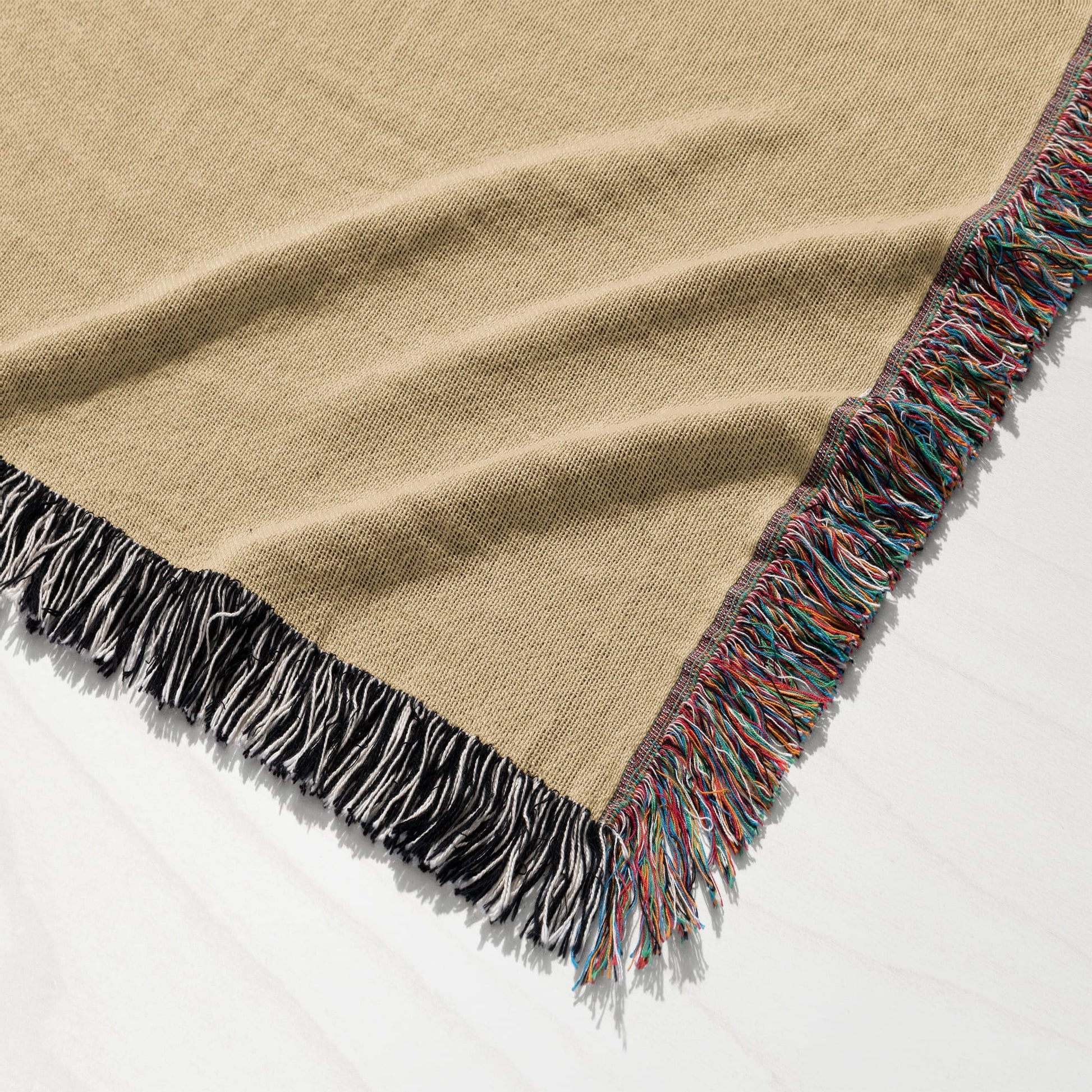 Beige woven throw blanket with colorful fringed edges on a white surface.
