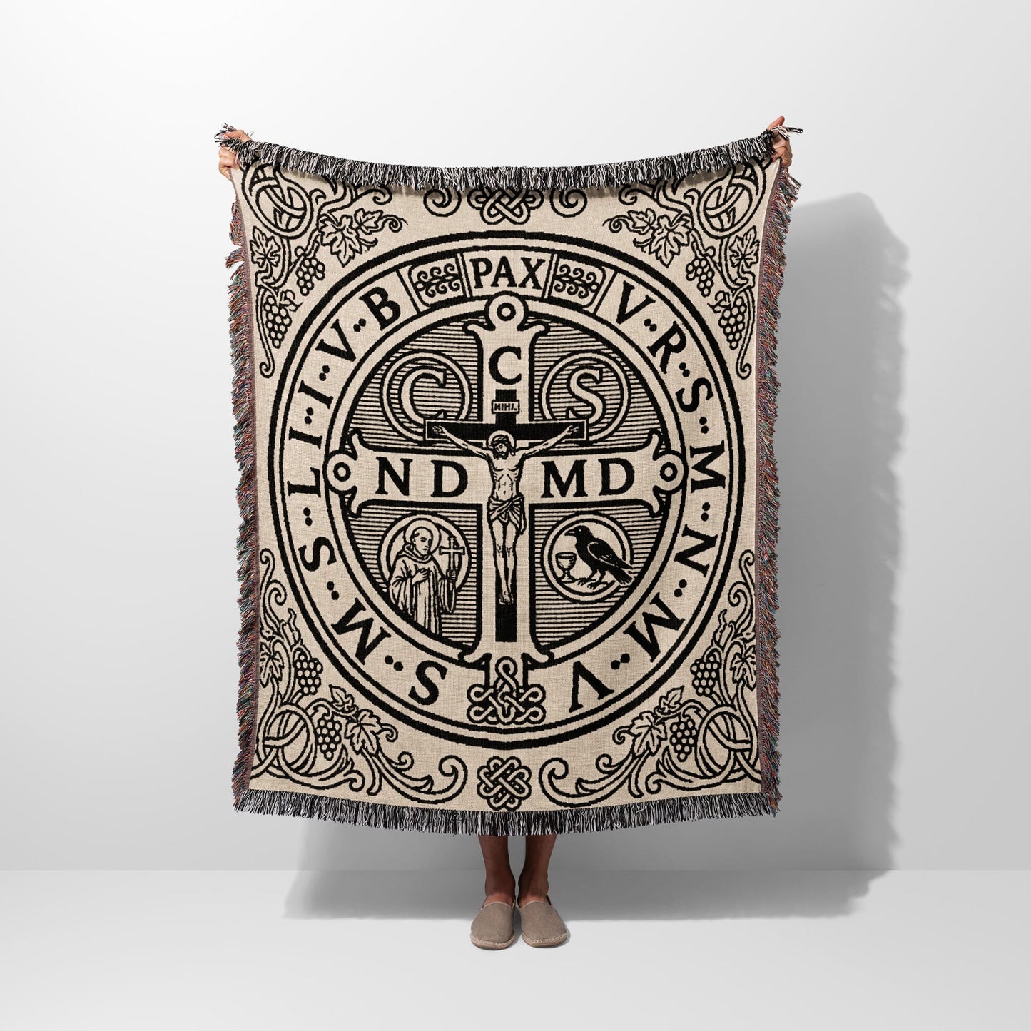 Woven blanket with St. Benedict medal design and fringe trim.