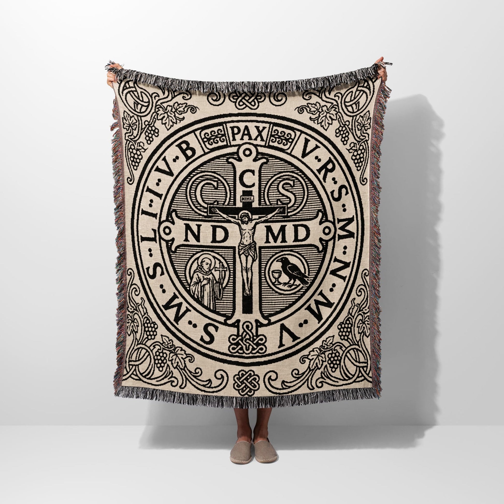 Woven blanket with St. Benedict medal design and fringe trim.