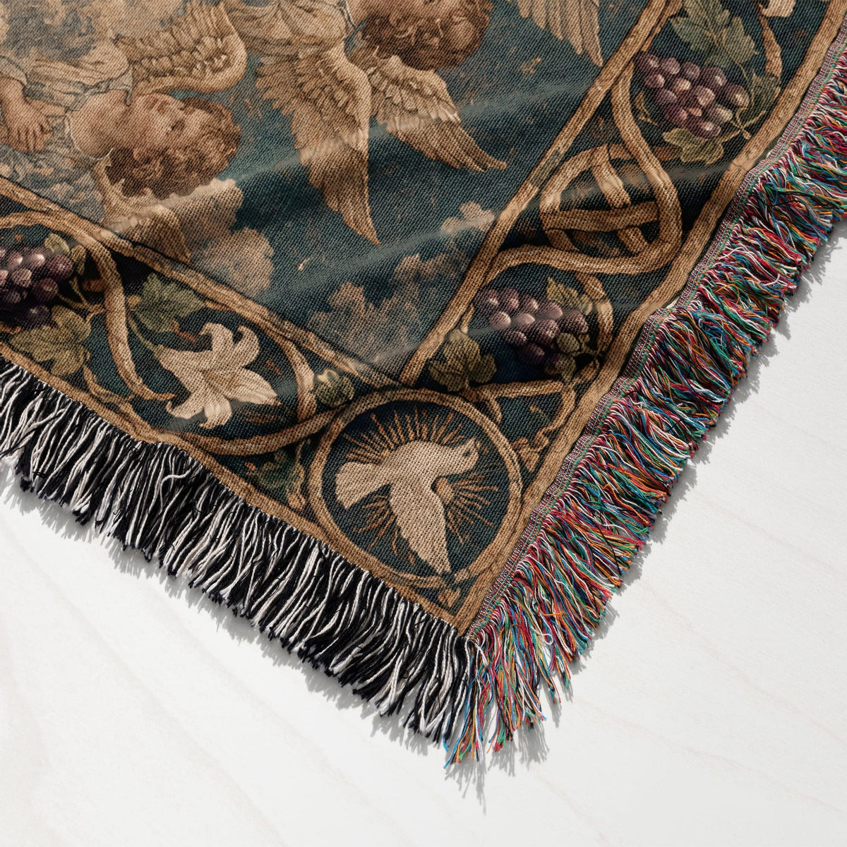 A folded woven tapestry featuring classical cherubs, grapevines, and a dove, finished with multicolored fringe.