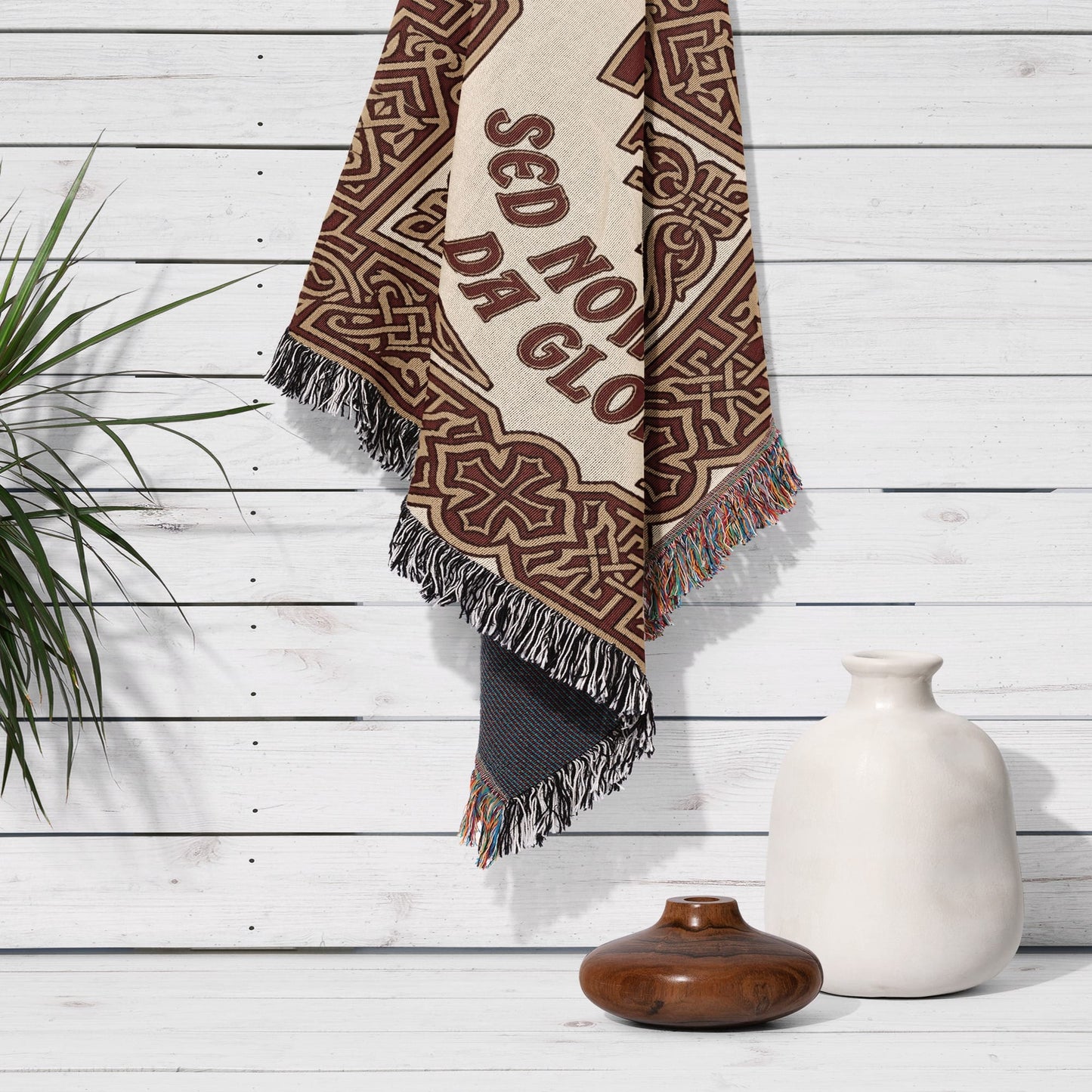 Woven tapestry with ornate pattern and "SED NO GLORIA" text hanging on white wood wall.
