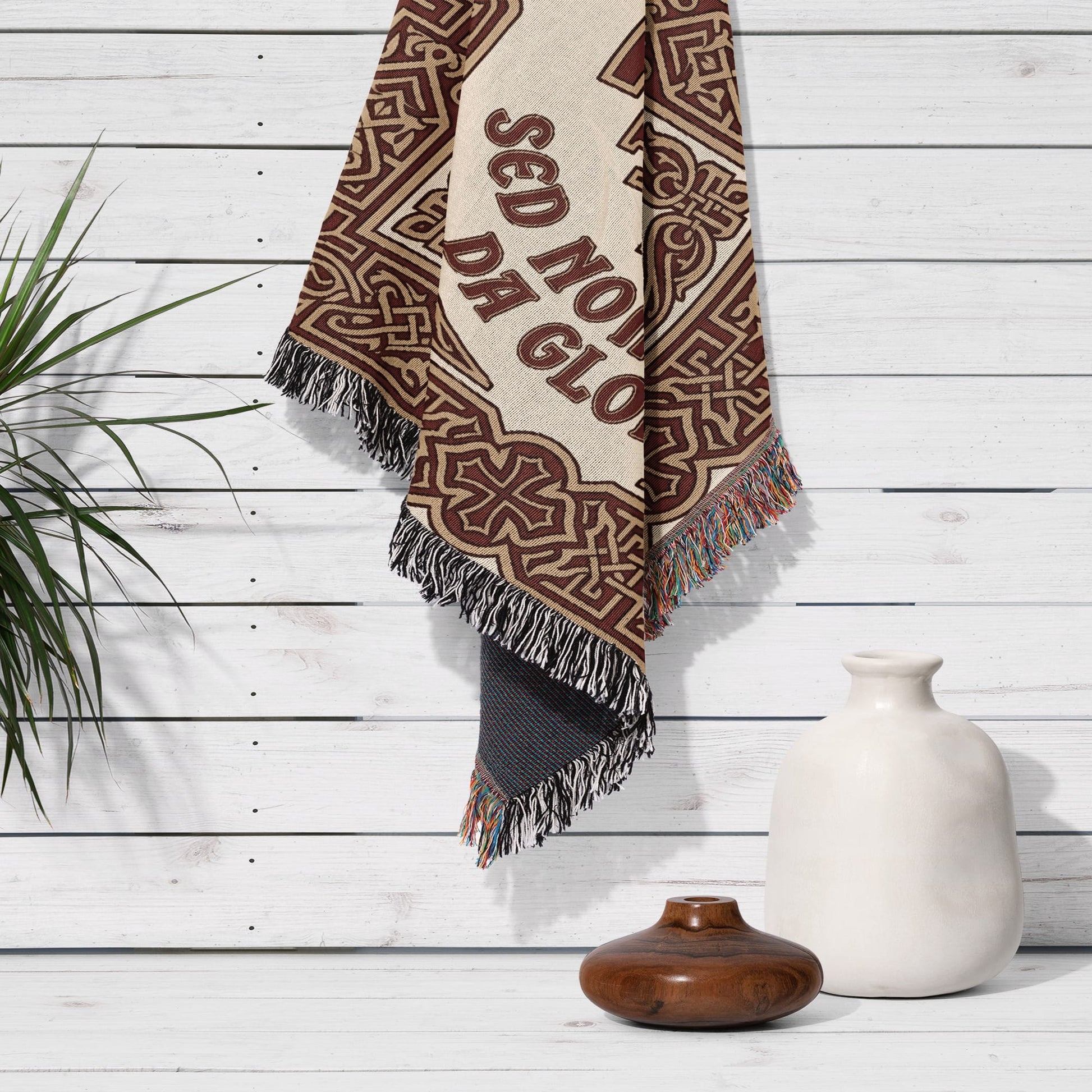 Woven tapestry with ornate pattern and "SED NO GLORIA" text hanging on white wood wall.