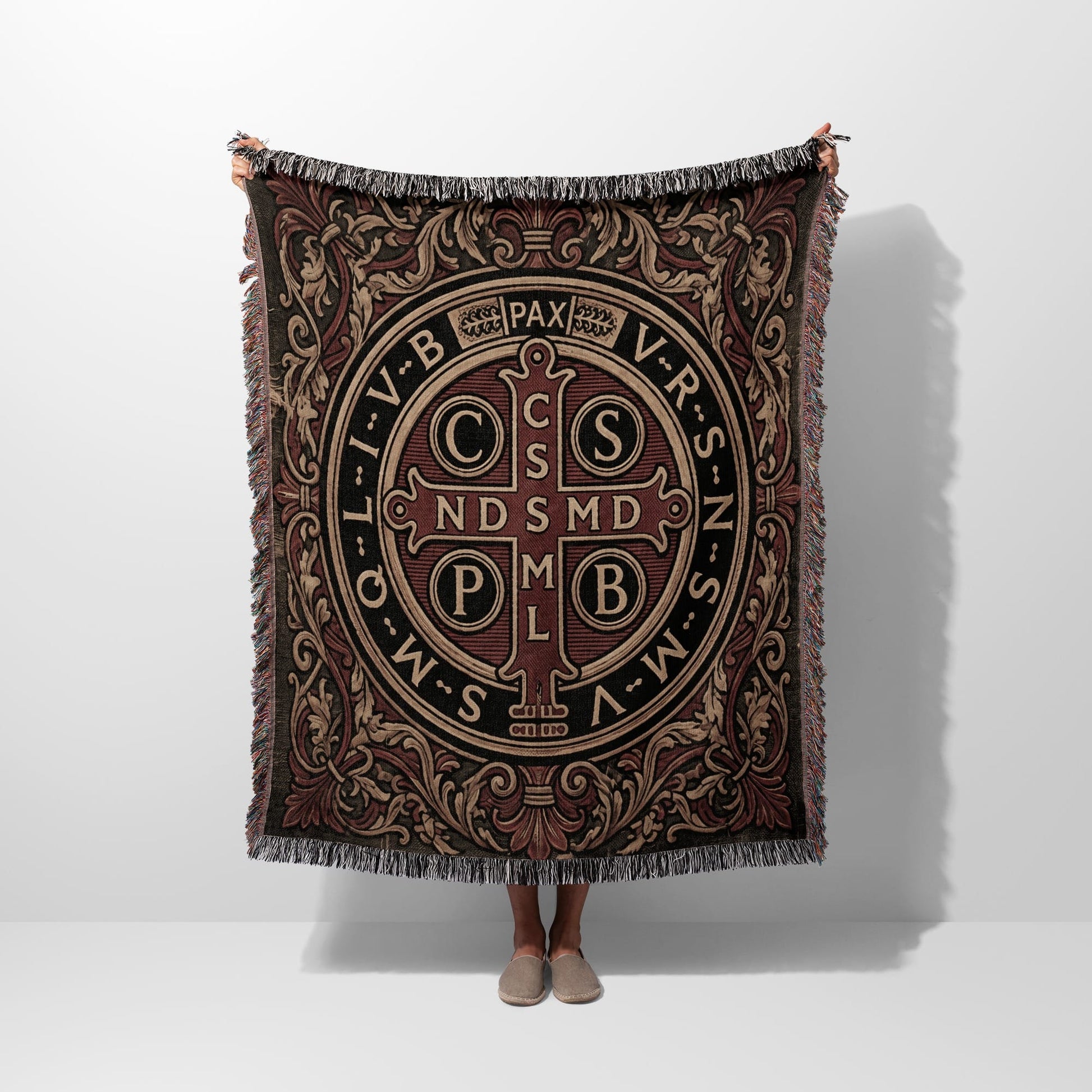 Woven throw blanket with Saint Benedict medal design and fringe trim.