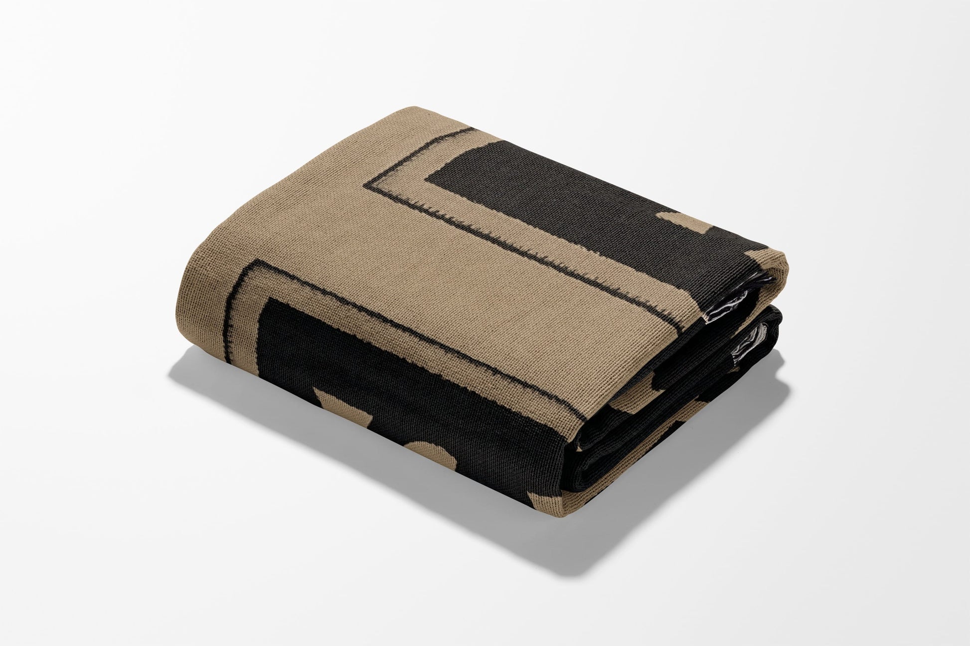 Folded beige blanket with a black geometric pattern.