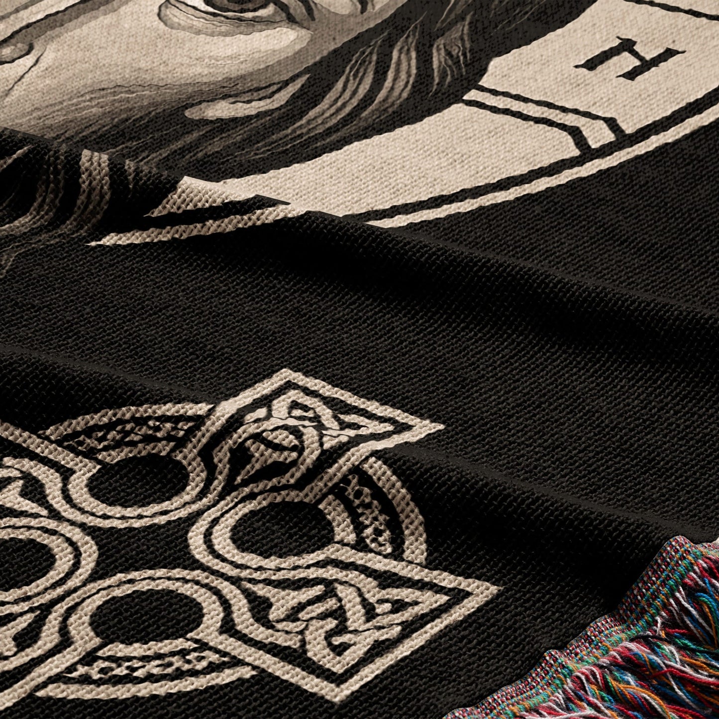 Woven blanket featuring a black background with a Celtic knot design and a partial portrait.