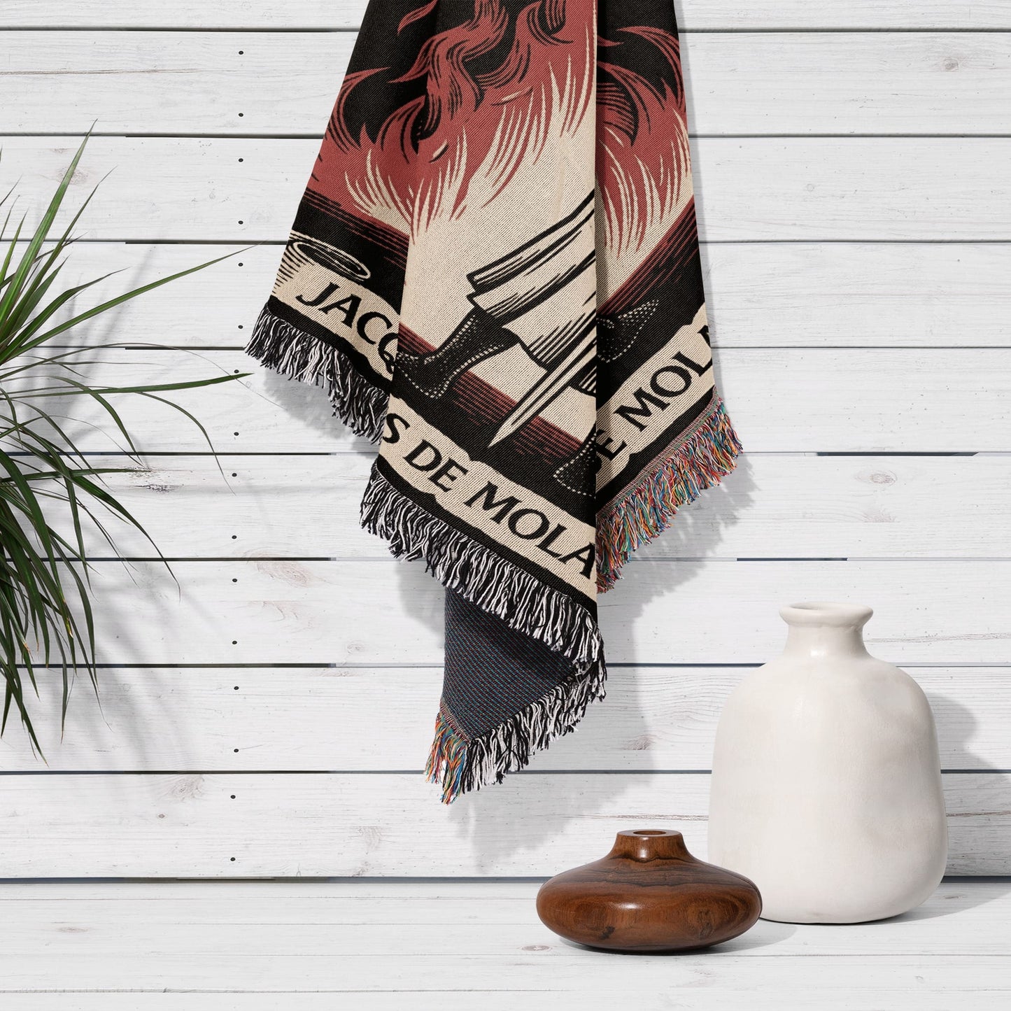 Woven blanket with "JACQUES DE MOLA" text and fringed edges hangs on a wall.