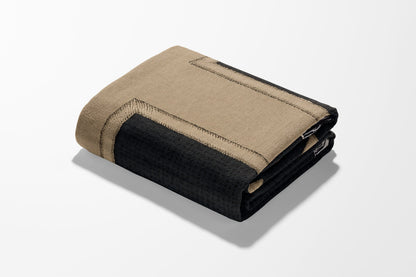 Folded tan and black throw blanket with textured trim.