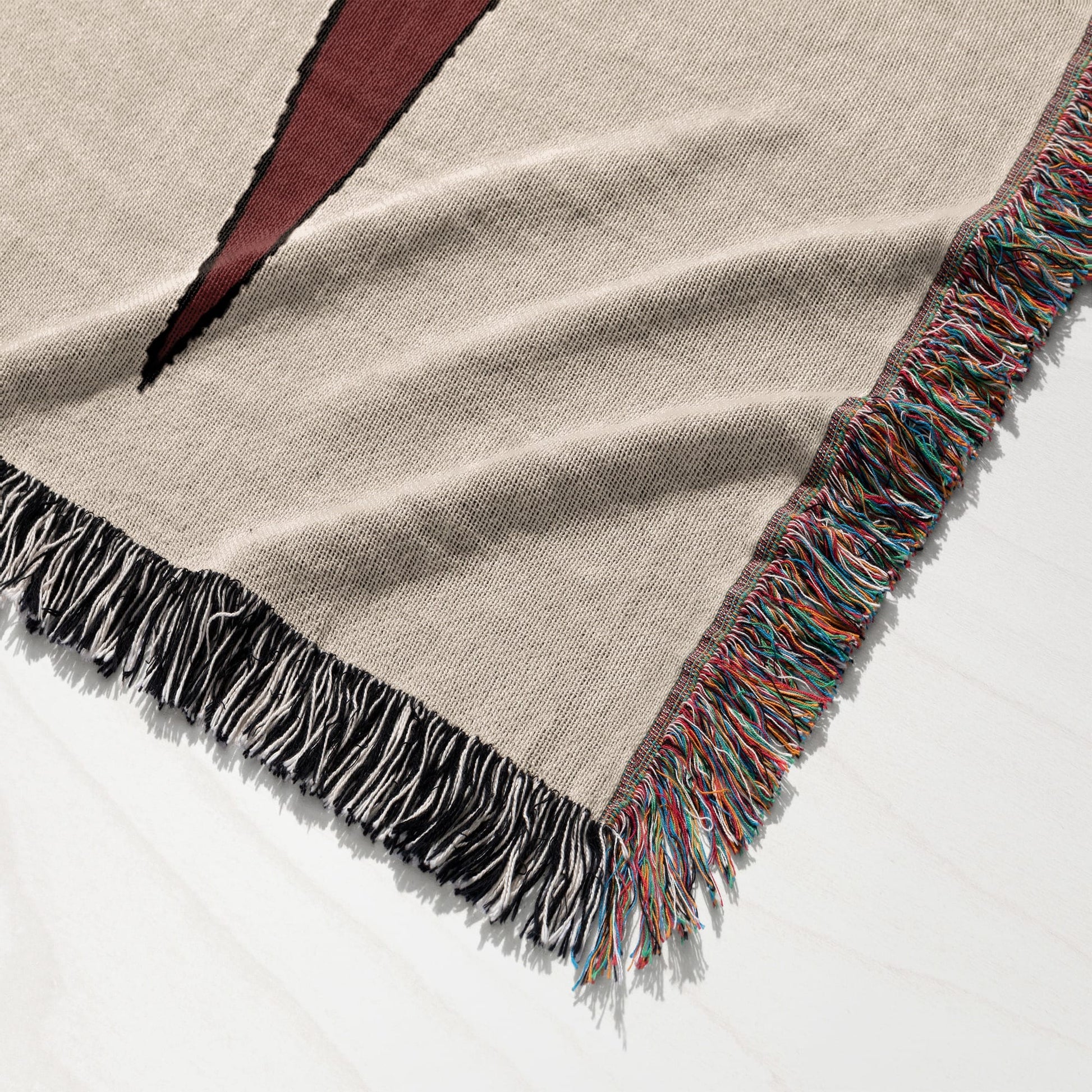 Beige woven blanket with colorful fringed edges and a black geometric design.