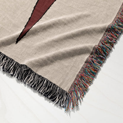 Beige woven blanket with colorful fringed edges and a black geometric design.