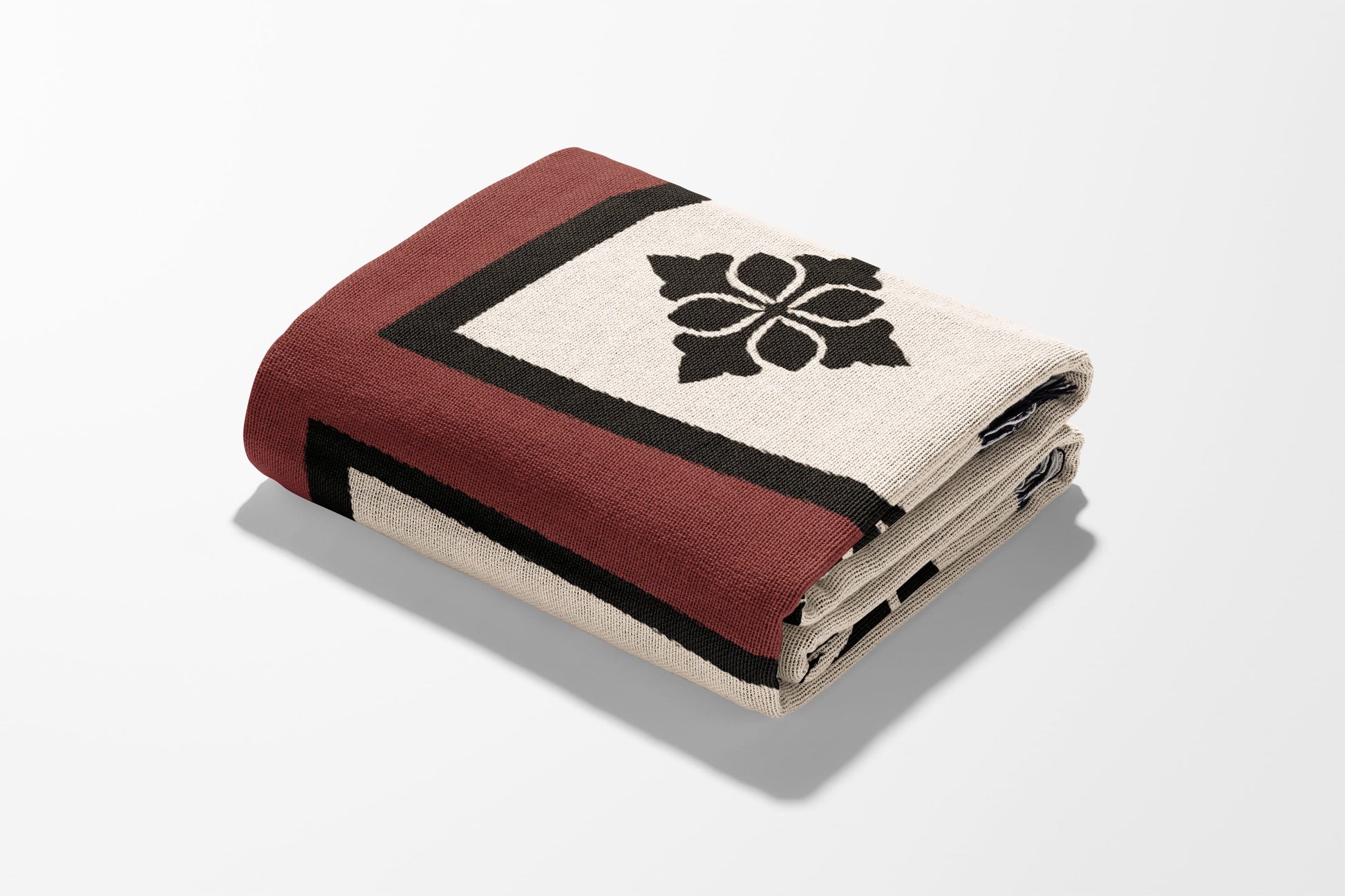 Folded blanket with a black floral design on a cream background and a maroon border.