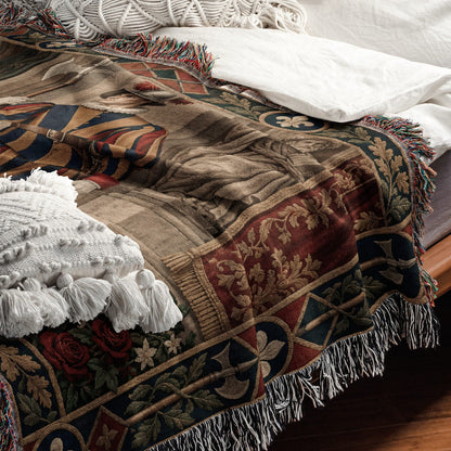 Woven throw blanket featuring a medieval-style portrait and floral borders, draped across a white-sheeted bed.