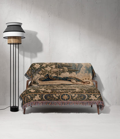 A wooden sofa draped in a detailed, medieval-style tapestry featuring floral patterns and a reclining figure.