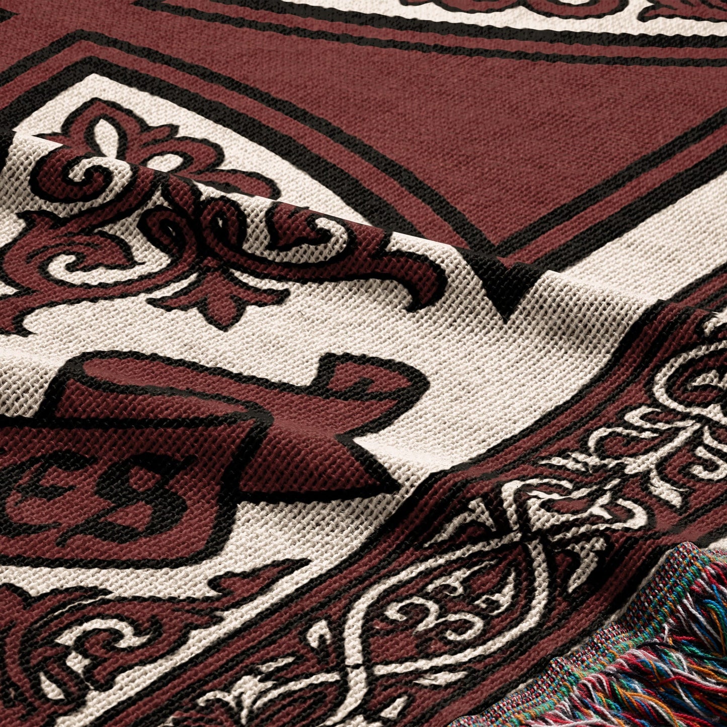 Maroon and cream woven blanket with ornate border and fringe detail.