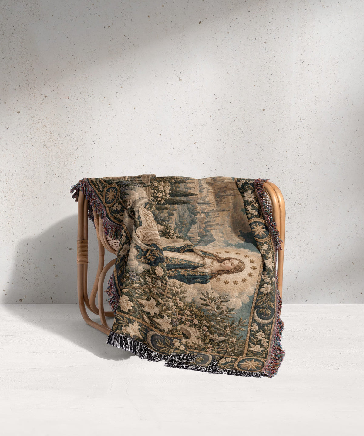 A woven tapestry blanket with a Renaissance art design draped over a rattan chair.