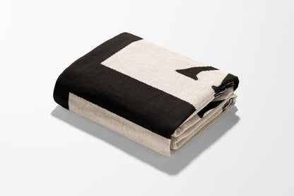 Folded black and cream blanket with letter 'L' design.