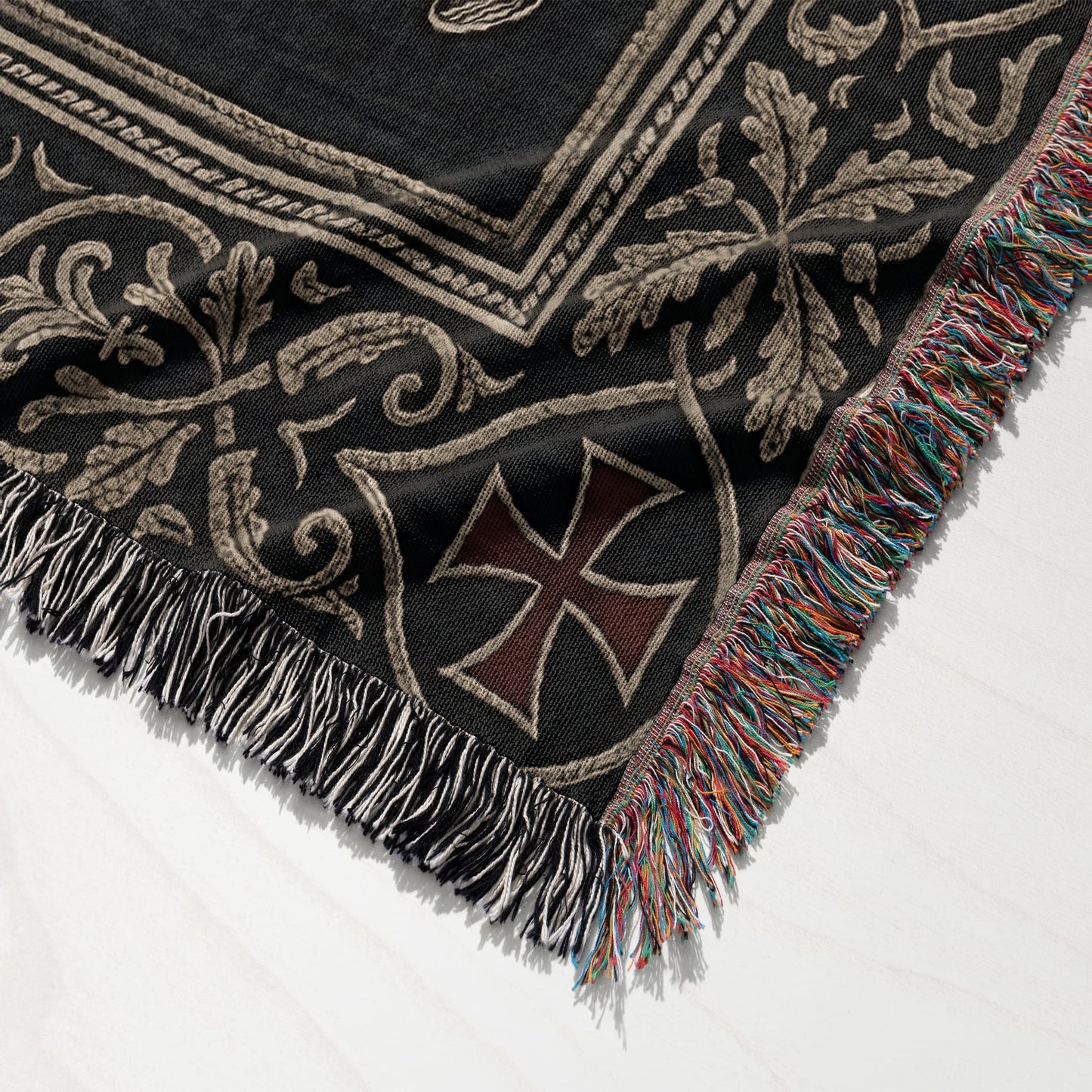 Black throw blanket with intricate tan scrollwork and a red cross emblem.