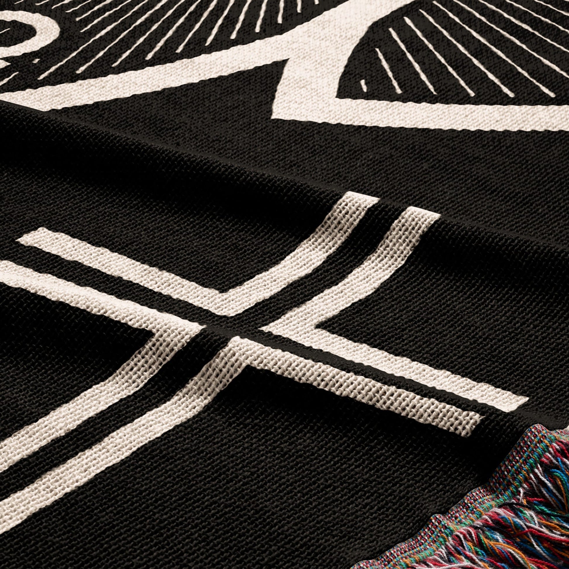 Black woven throw with white geometric pattern and colorful fringed edge.