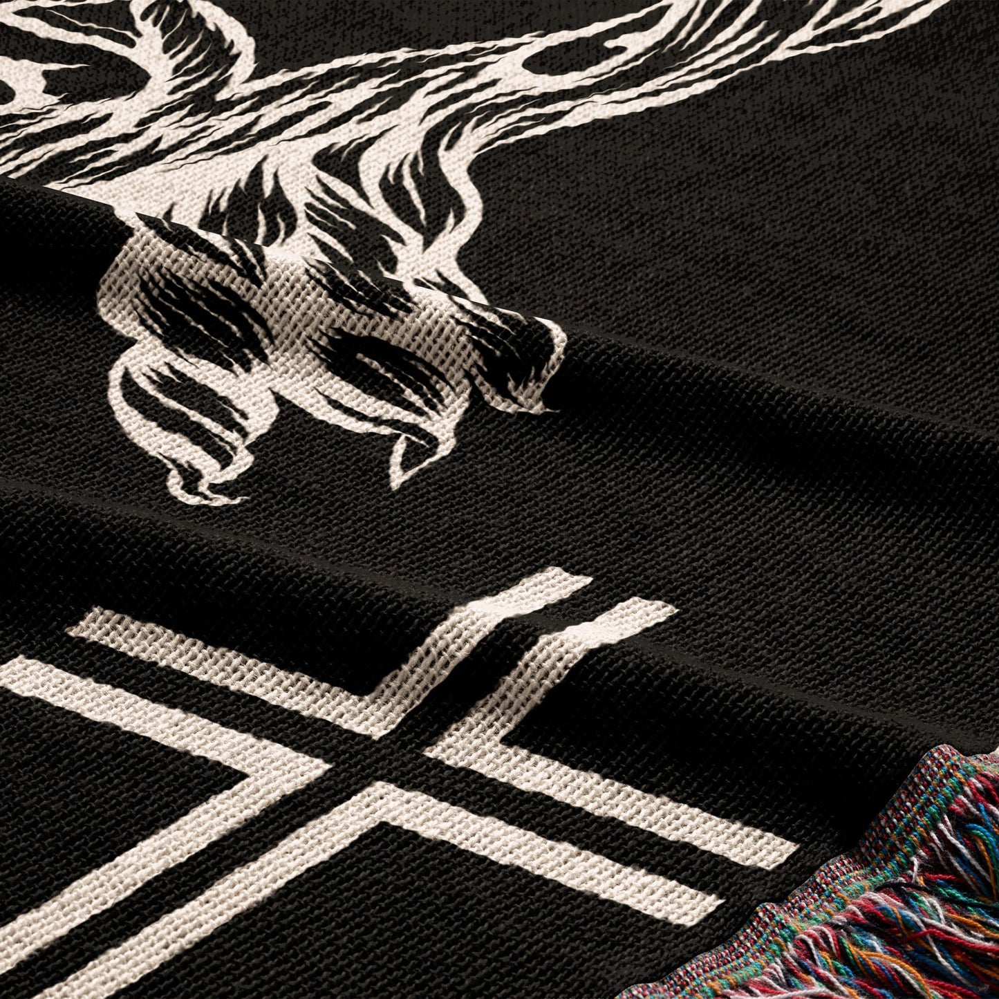 Black knitted throw blanket with white skull and crossbones graphic and fringe.