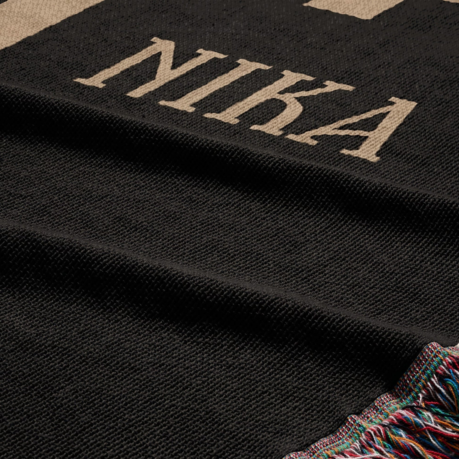 Black woven blanket with beige "NIKA" text and fringed edge.