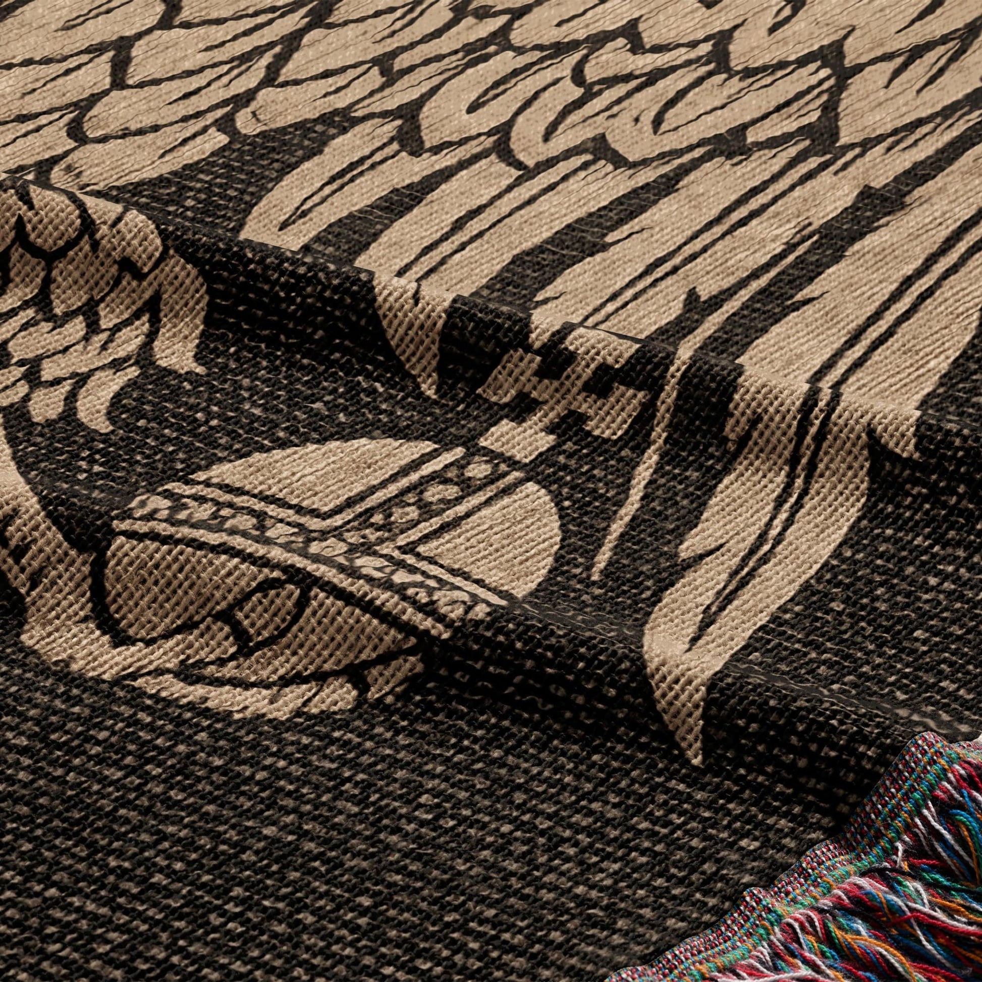 Close-up of a woven blanket with a detailed crest pattern and colorful fringed edge.