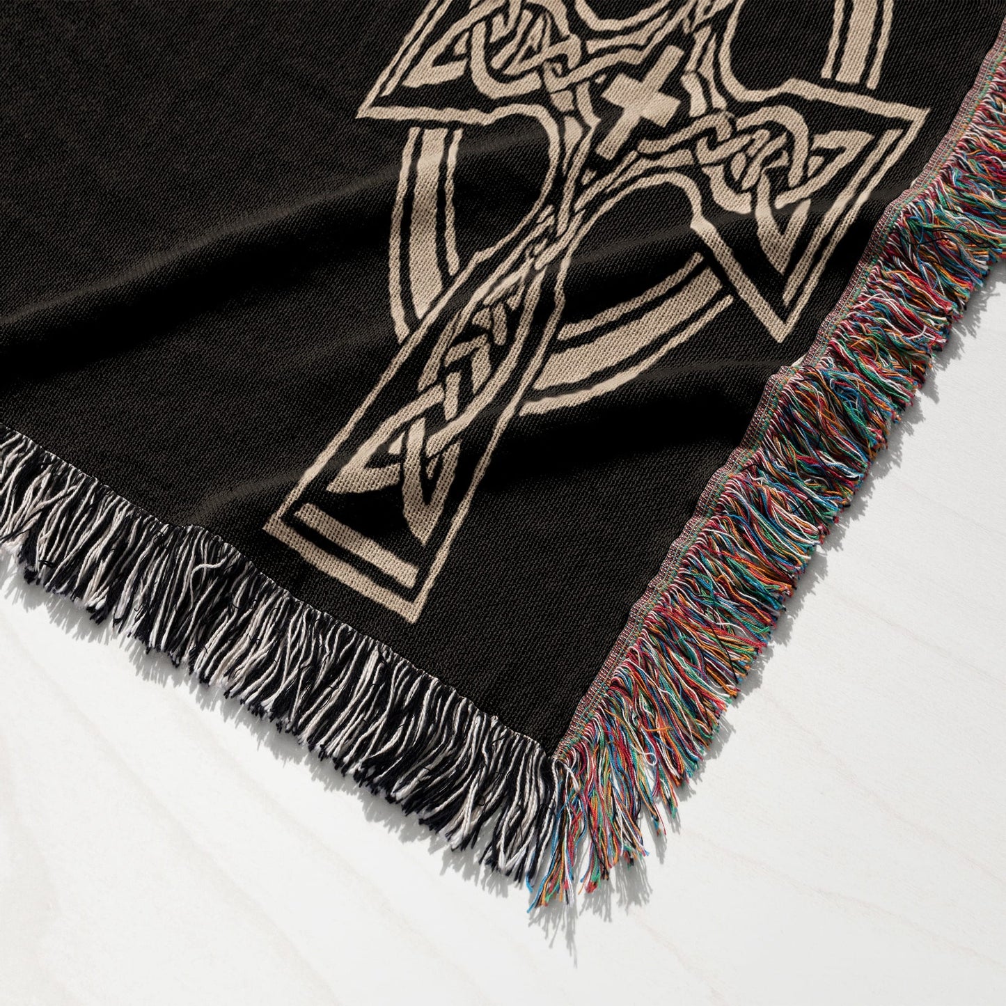 Black woven blanket with a beige Celtic knot cross design and fringed edges.