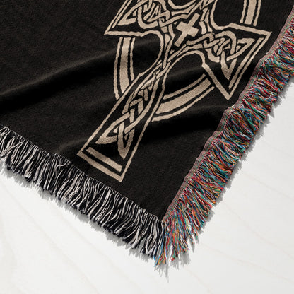 Black woven blanket with a beige Celtic knot cross design and fringed edges.