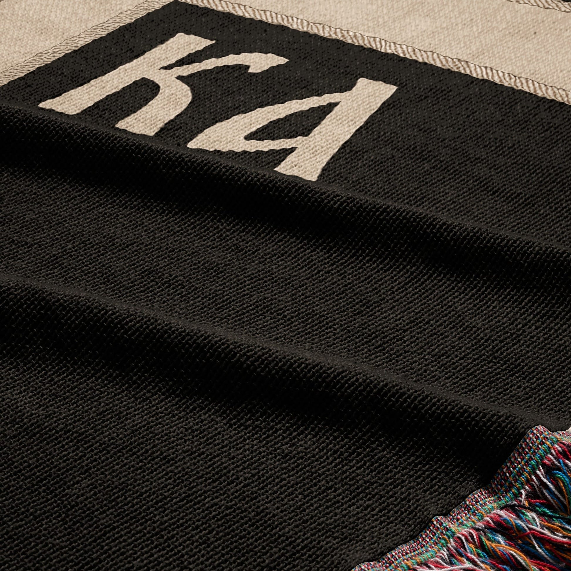 Black textured blanket with "KA" logo and colorful fringed edge.