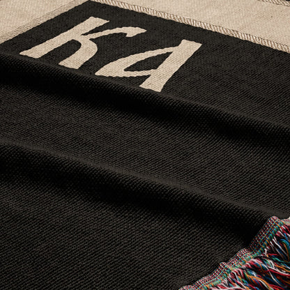 Black textured blanket with "KA" logo and colorful fringed edge.