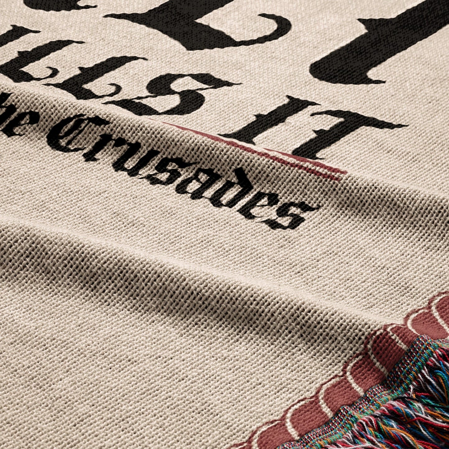 Close-up of a woven blanket with black text reading "the Crusades" and fringed edge.
