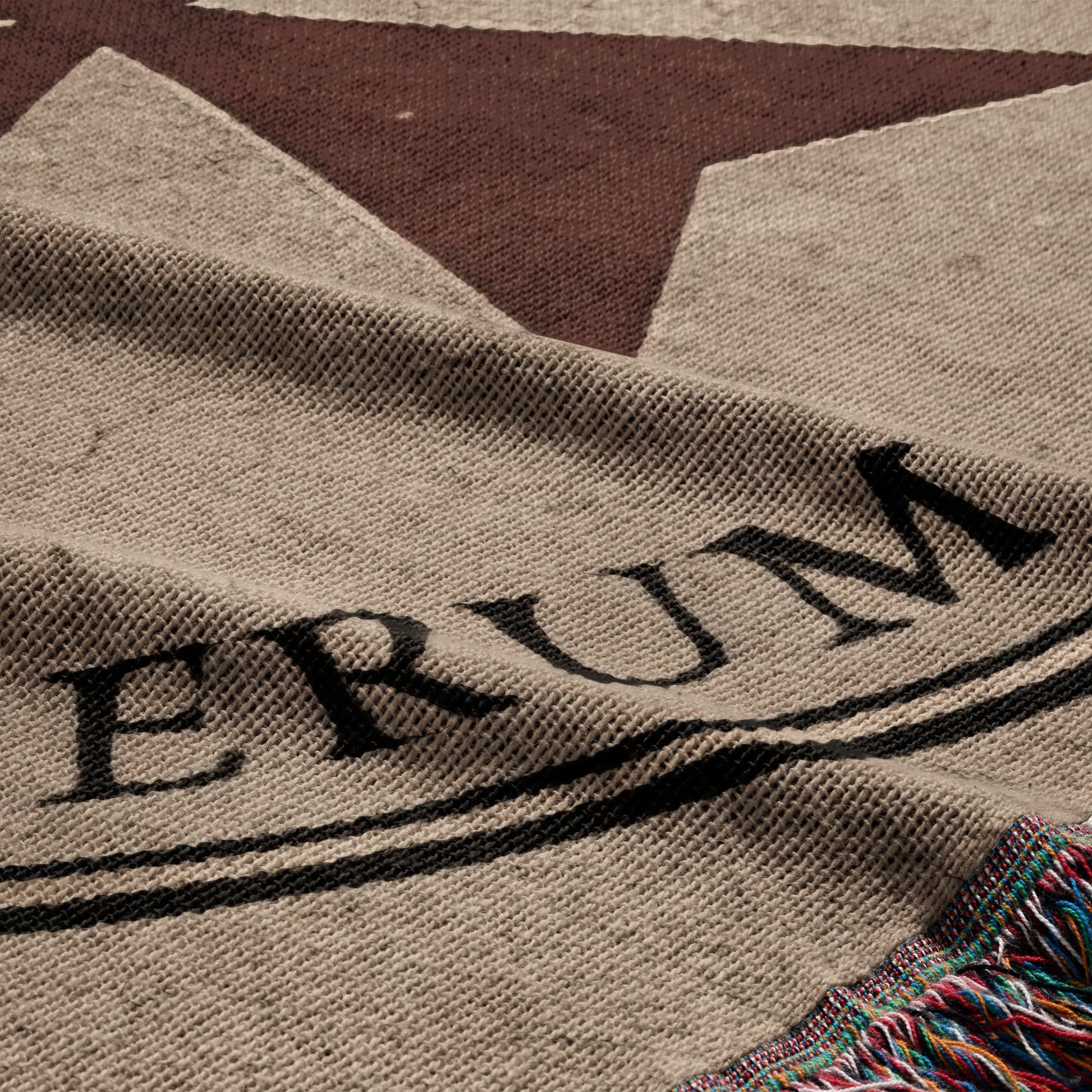 Tan throw with black lettering "ERUM" and colorful fringed edge.