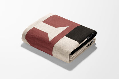 Folded blanket with geometric pattern in red, cream, and black.