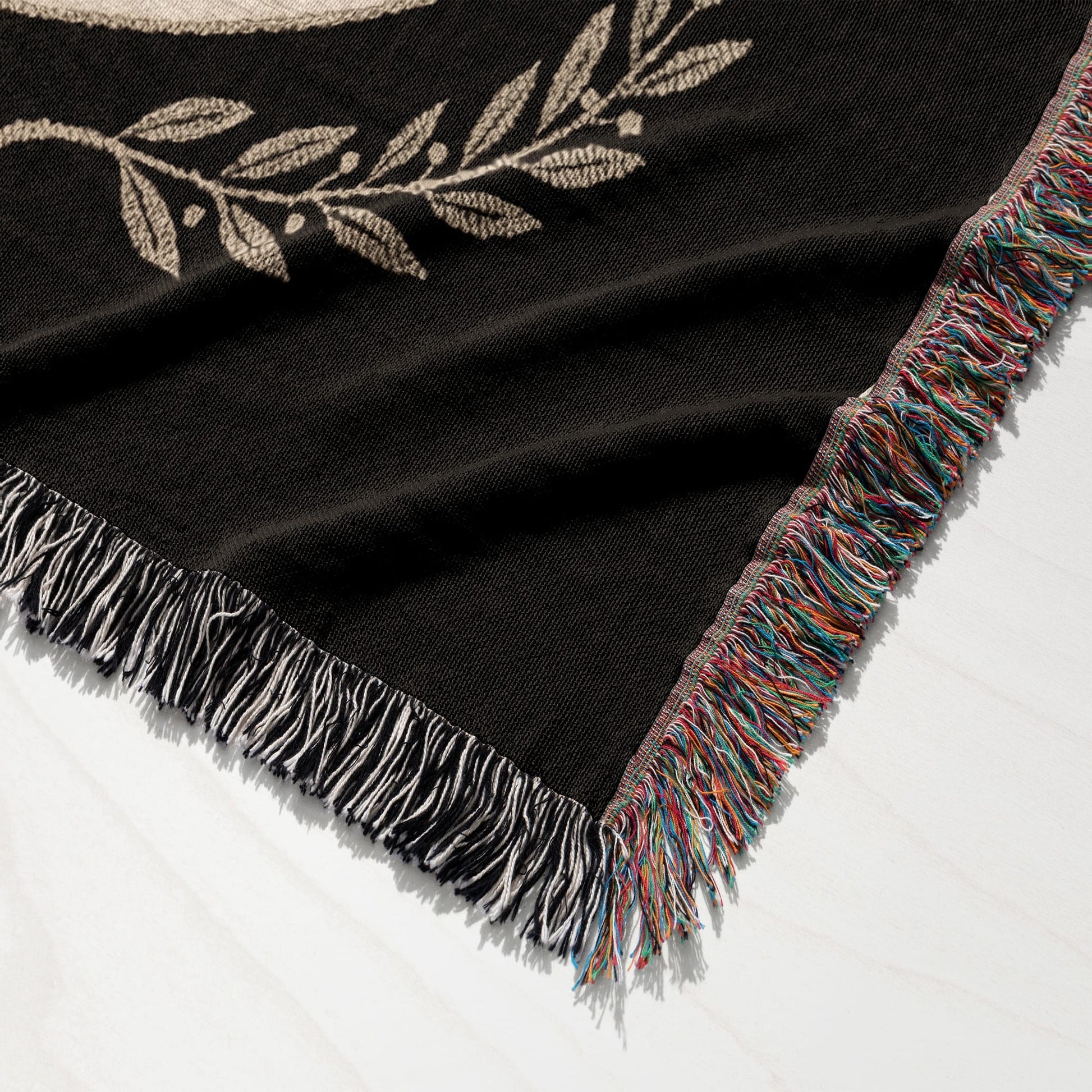 Black woven throw blanket with fringed edges and an embroidered laurel wreath detail.
