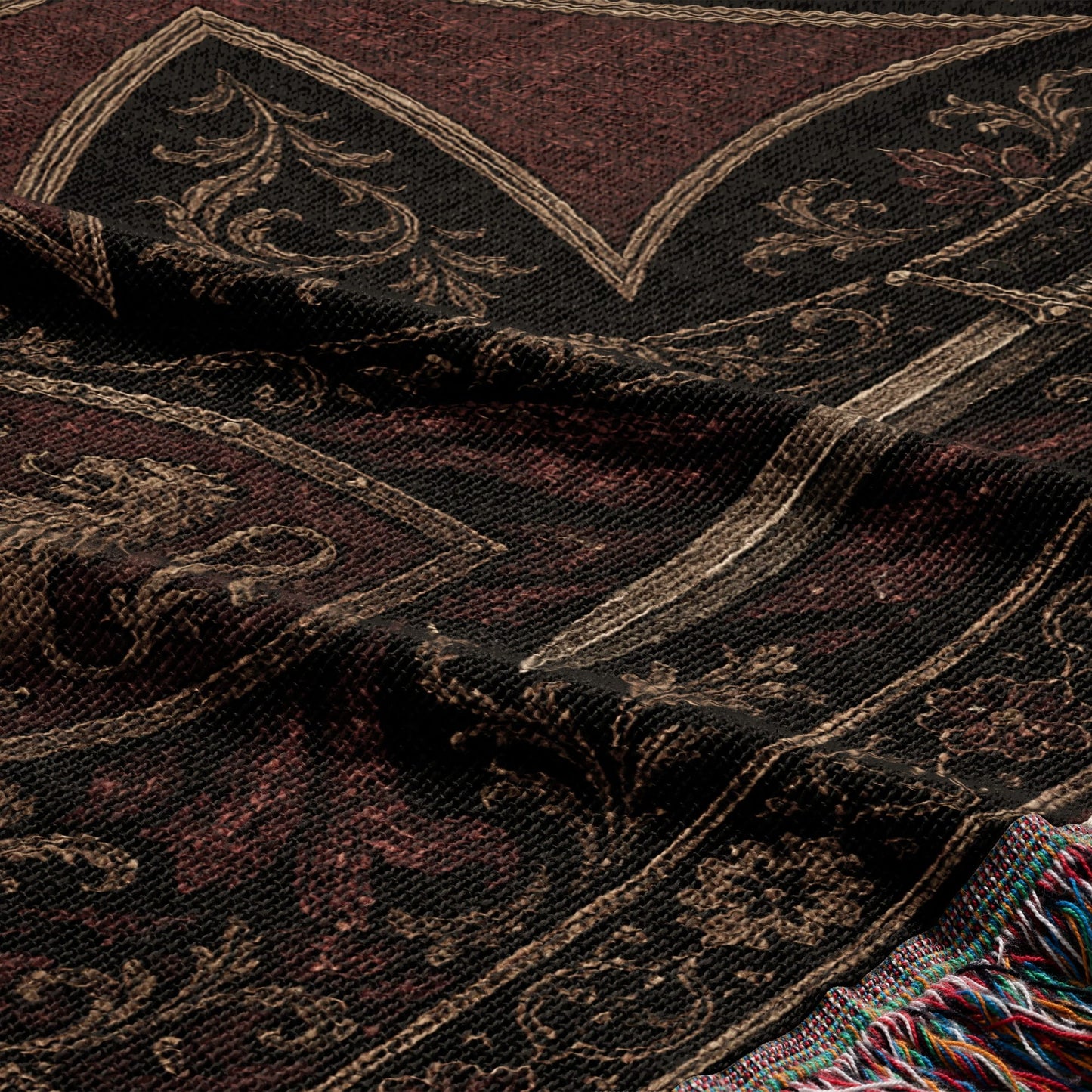 Dark brown and red textile with ornate gold and black woven pattern and tasseled edge.