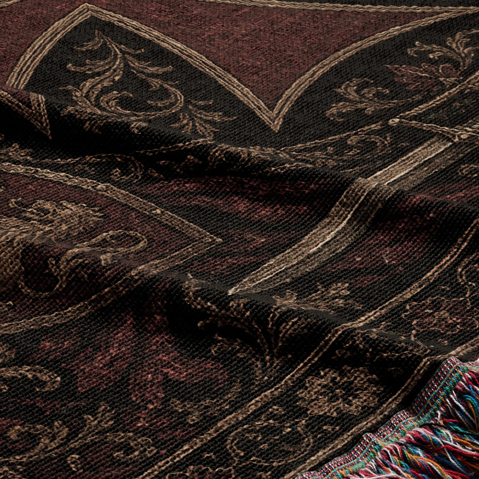 Dark brown and red textile with ornate gold and black woven pattern and tasseled edge.