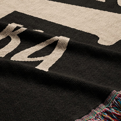 Black and cream knit blanket with fringe, showing partial text.