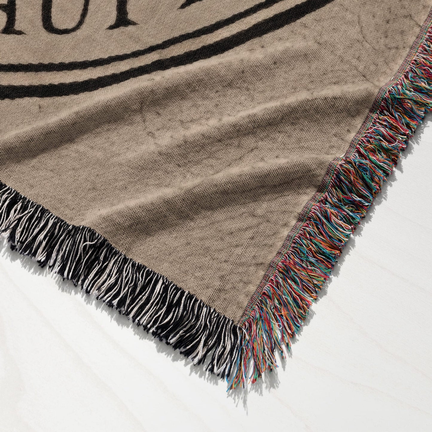 Woven blanket with tan background, black stripe pattern, and multicolored fringe.