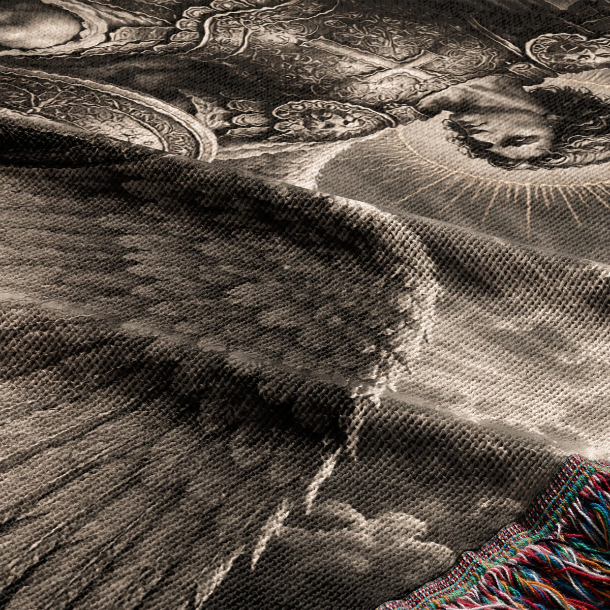 A textured woven blanket with a sepia-toned classical artistic print and colorful fringe.