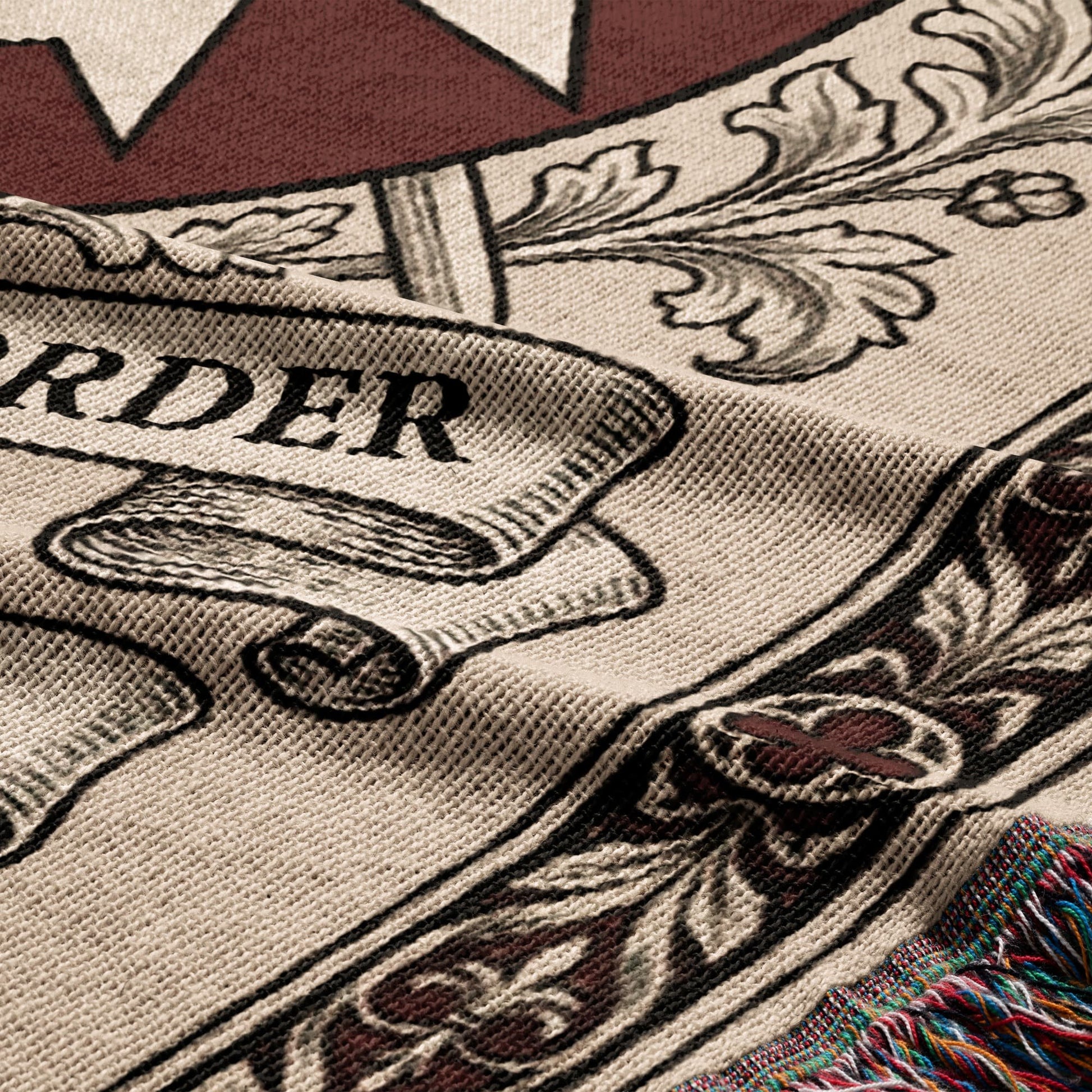Woven blanket with floral, scroll, and text "ORDER" design and fringed edge.