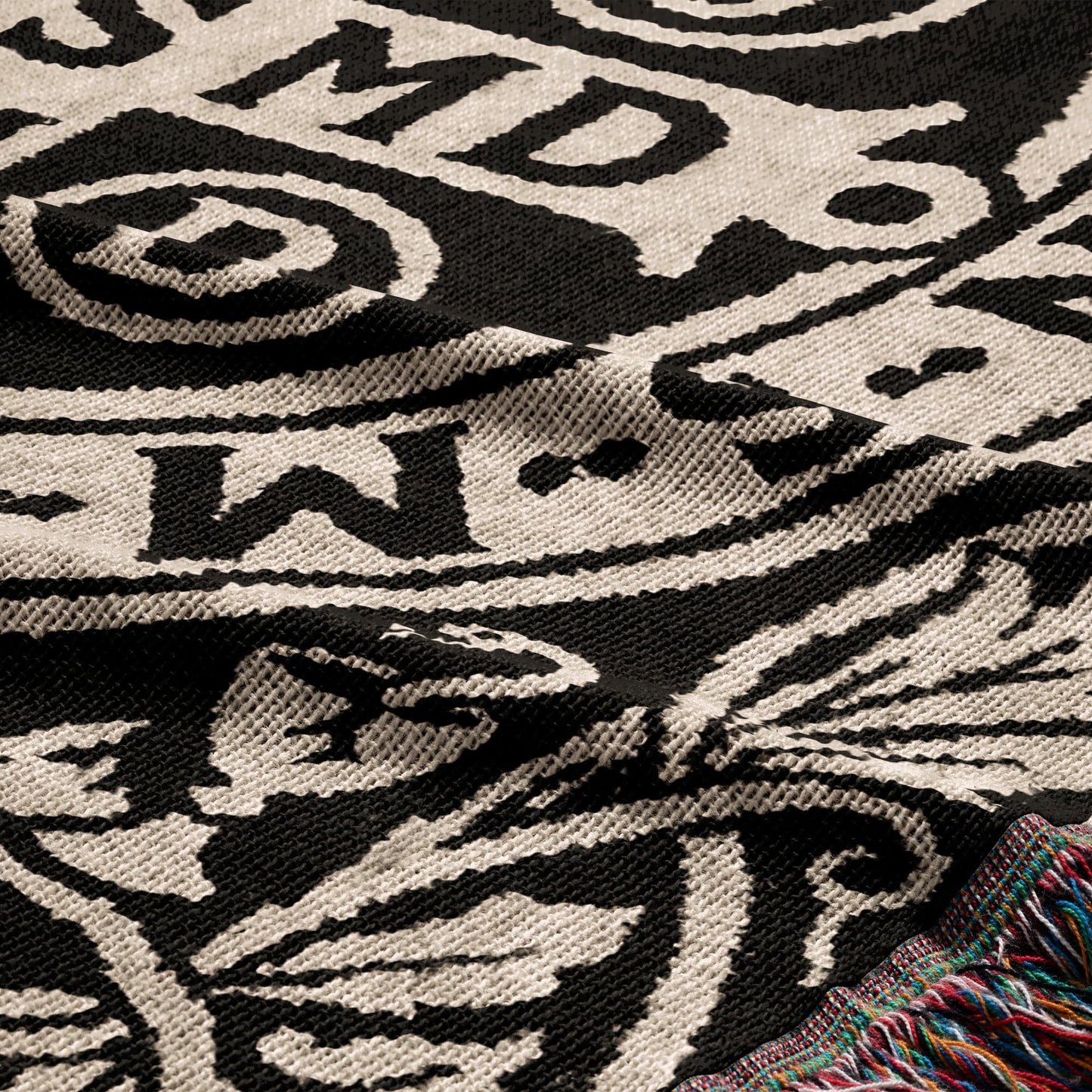 Woven blanket with a black and white tribal pattern and colorful fringed edge.