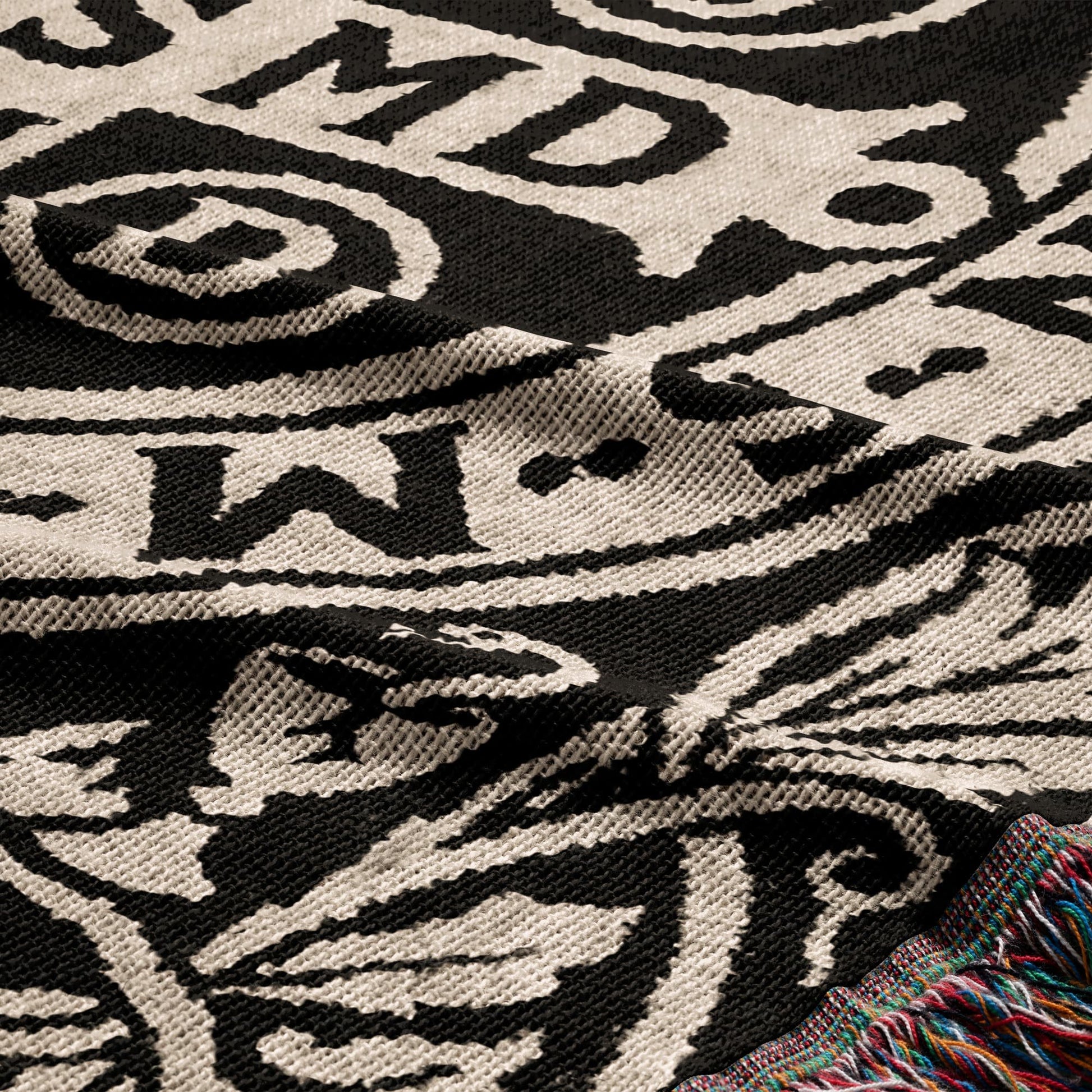 Woven blanket with a black and white tribal pattern and colorful fringed edge.